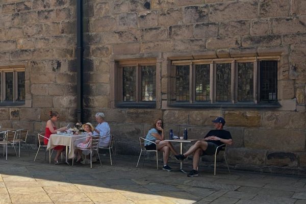 Visitors relaxing outside the Hoghton Tower Tearoom in Lancashire, enjoying tea and cake in the sunshine with views of the historic gardens.